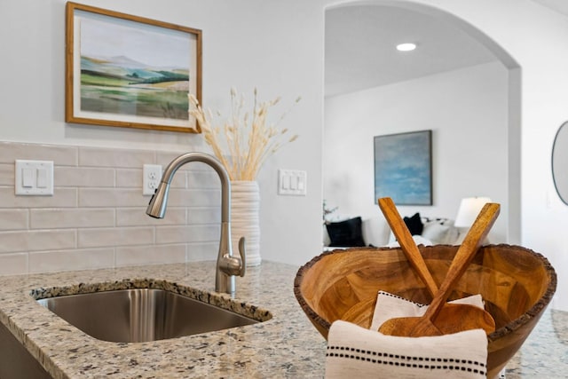 room details featuring backsplash, light stone countertops, and sink