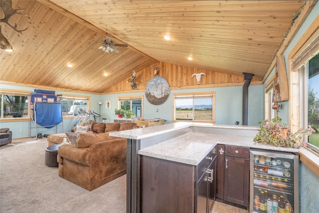 kitchen with wooden ceiling, a wood stove, wine cooler, light colored carpet, and dark brown cabinetry