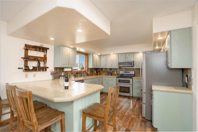 kitchen featuring backsplash, a breakfast bar, kitchen peninsula, dark wood-type flooring, and stainless steel appliances