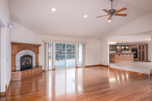 unfurnished living room featuring ceiling fan, a tiled fireplace, light hardwood / wood-style flooring, and high vaulted ceiling