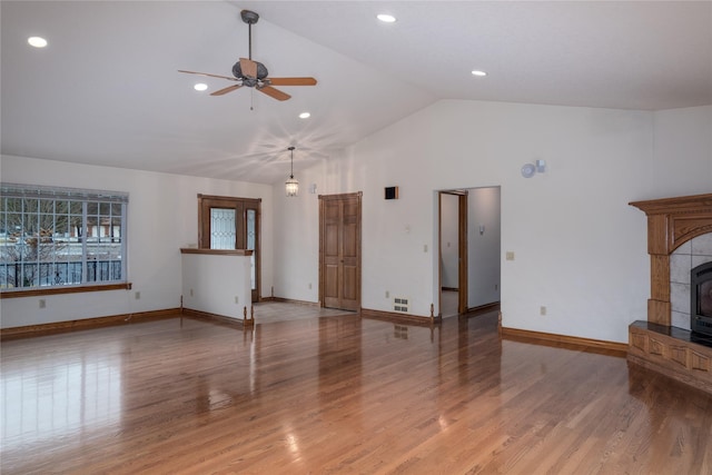 unfurnished living room featuring ceiling fan, vaulted ceiling, a wood stove, and hardwood / wood-style floors