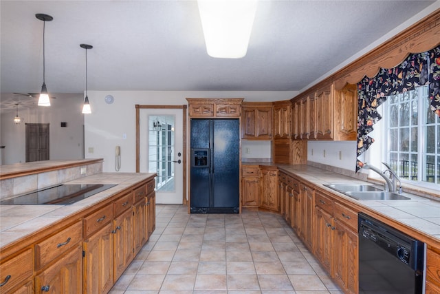 kitchen with tile counters, decorative light fixtures, black appliances, and sink