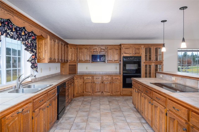 kitchen with black appliances, sink, hanging light fixtures, plenty of natural light, and tile countertops