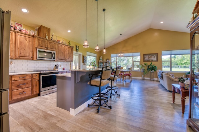 kitchen with appliances with stainless steel finishes, decorative light fixtures, decorative backsplash, light stone counters, and a breakfast bar area