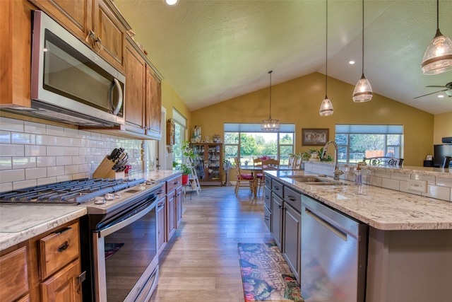 kitchen with decorative light fixtures, sink, appliances with stainless steel finishes, and a center island with sink