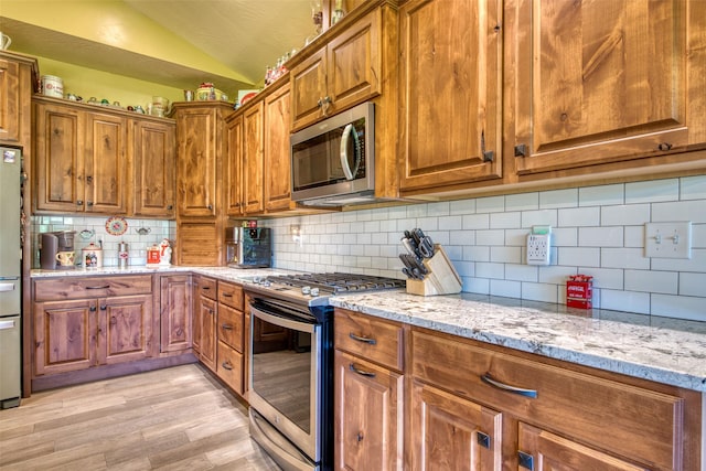 kitchen with stainless steel appliances, tasteful backsplash, lofted ceiling, light hardwood / wood-style flooring, and light stone counters