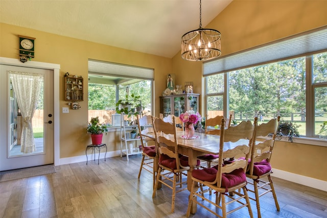 dining room featuring lofted ceiling, a healthy amount of sunlight, wood-type flooring, and a chandelier