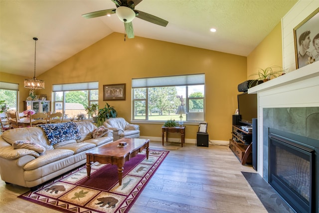 living room featuring vaulted ceiling, a tile fireplace, ceiling fan with notable chandelier, and light hardwood / wood-style flooring