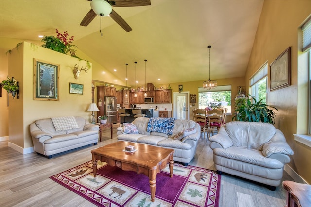 living room with ceiling fan with notable chandelier, light hardwood / wood-style floors, and high vaulted ceiling