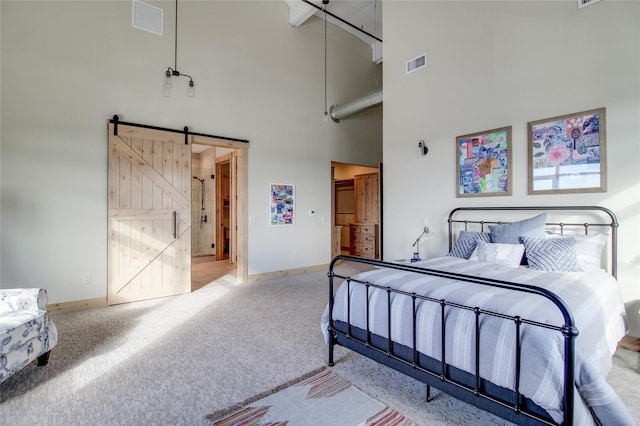 carpeted bedroom with ensuite bath, a barn door, and a high ceiling