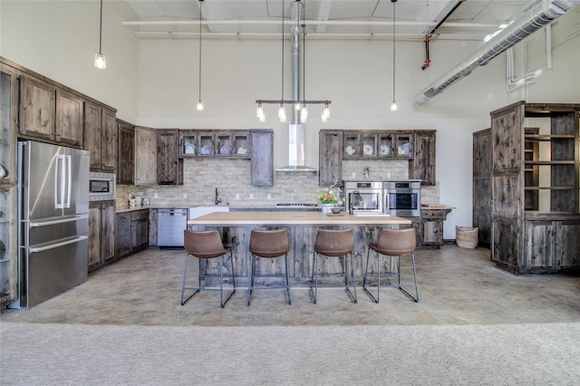 kitchen featuring wall chimney exhaust hood, dark brown cabinets, stainless steel appliances, and a center island with sink