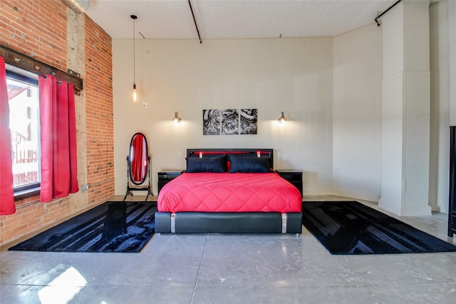 bedroom featuring concrete floors, a high ceiling, and brick wall