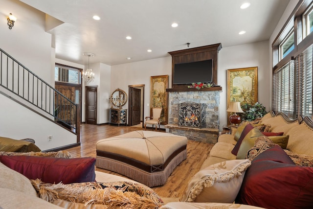 living room with a notable chandelier, a stone fireplace, and hardwood / wood-style flooring