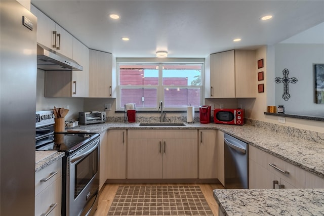 kitchen with light stone countertops, appliances with stainless steel finishes, light hardwood / wood-style floors, sink, and light brown cabinetry