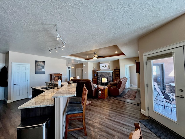 kitchen featuring dark wood-type flooring, a fireplace, a tray ceiling, a center island with sink, and a breakfast bar area