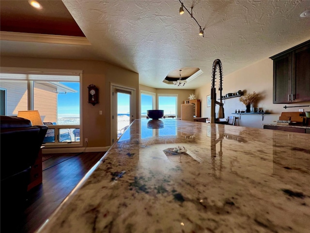 interior space with a raised ceiling, a notable chandelier, a textured ceiling, and dark wood-type flooring