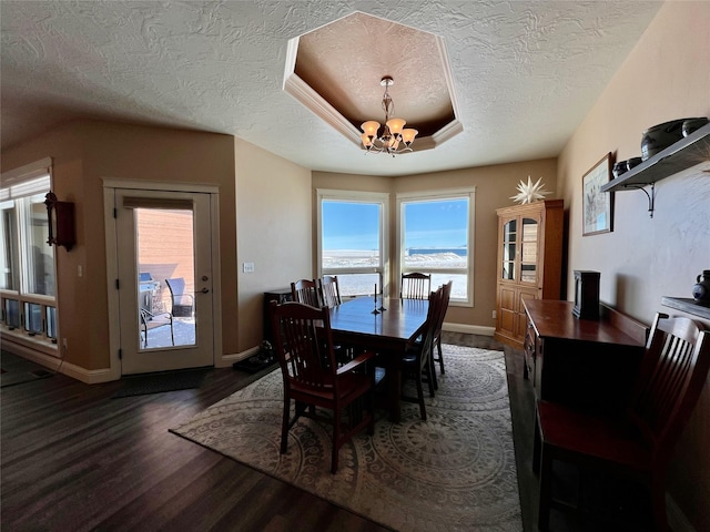 dining room with a tray ceiling, dark wood-type flooring, a textured ceiling, a water view, and a chandelier