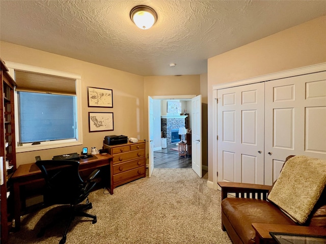 home office with a stone fireplace, a textured ceiling, and carpet flooring