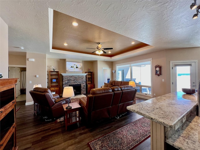 living room with a raised ceiling, ceiling fan, dark wood-type flooring, and a textured ceiling