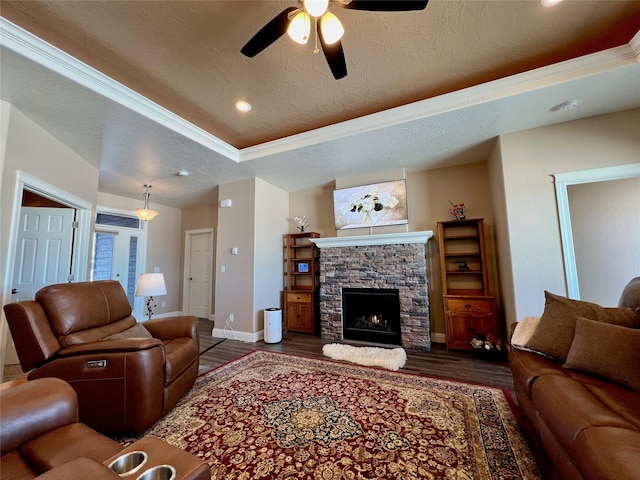 living room with dark wood-type flooring, ceiling fan, a fireplace, and a tray ceiling