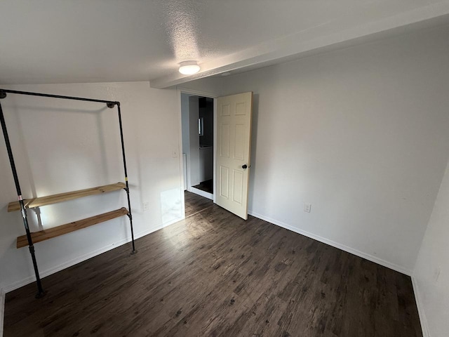 unfurnished bedroom with a textured ceiling, dark hardwood / wood-style flooring, and vaulted ceiling