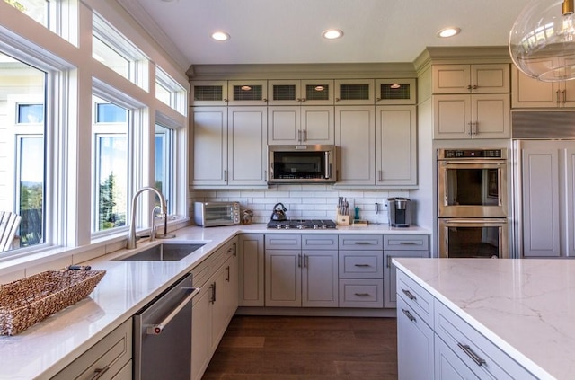 kitchen with stainless steel appliances, tasteful backsplash, decorative light fixtures, light stone counters, and sink