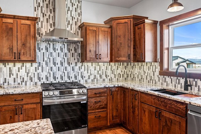 kitchen featuring light stone counters, tasteful backsplash, a sink, appliances with stainless steel finishes, and wall chimney exhaust hood