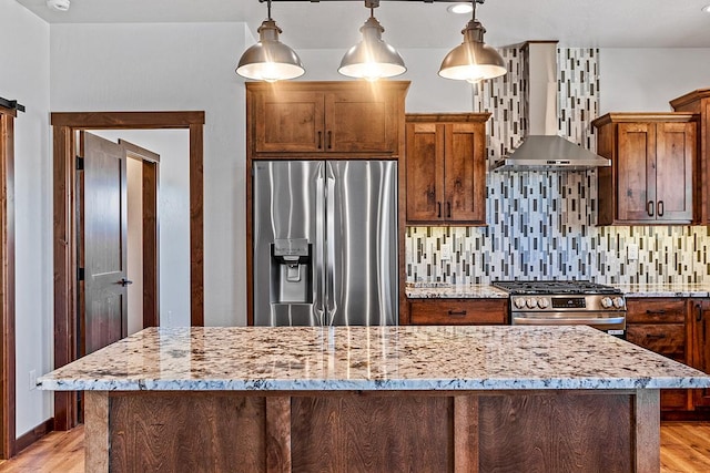 kitchen featuring light wood-type flooring, stainless steel appliances, wall chimney range hood, and decorative backsplash