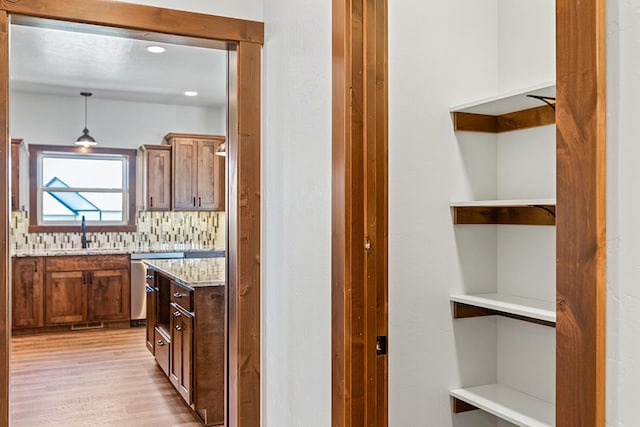 kitchen featuring a sink, light wood-style floors, open shelves, hanging light fixtures, and dishwasher