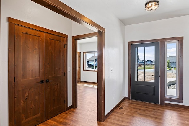 foyer entrance with baseboards, visible vents, and wood finished floors