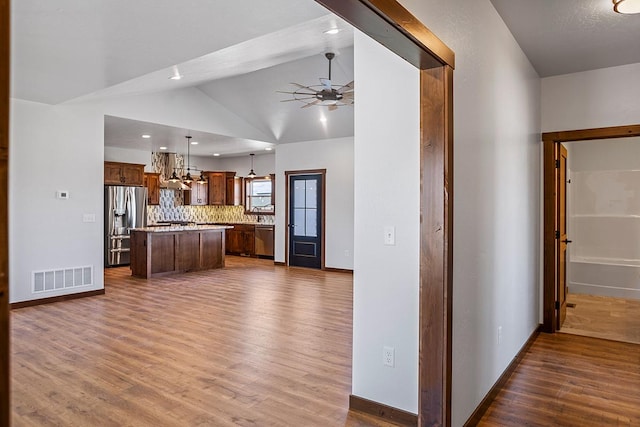 kitchen featuring visible vents, stainless steel appliances, dark wood-style floors, wall chimney exhaust hood, and ceiling fan with notable chandelier