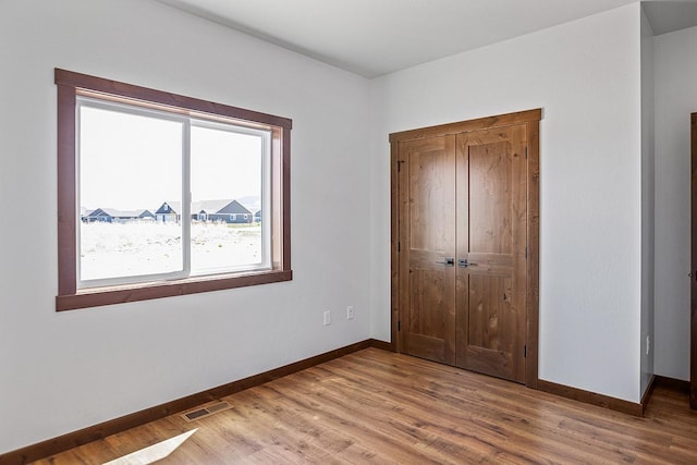 unfurnished bedroom with baseboards, visible vents, wood finished floors, and a closet