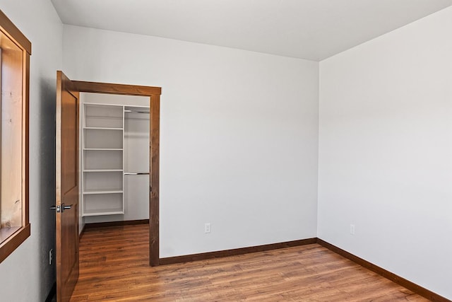 unfurnished bedroom with wood finished floors, a spacious closet, baseboards, and a closet