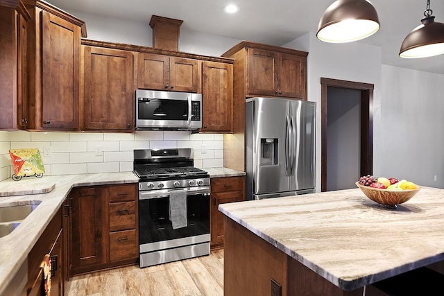 kitchen with light hardwood / wood-style floors, hanging light fixtures, appliances with stainless steel finishes, and decorative backsplash