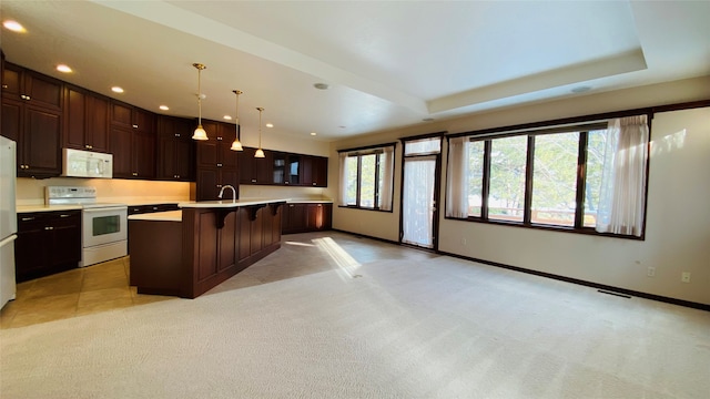 kitchen with light carpet, a kitchen bar, an island with sink, decorative light fixtures, and white appliances