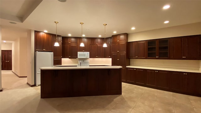 kitchen featuring pendant lighting, sink, white appliances, dark brown cabinetry, and a kitchen island with sink