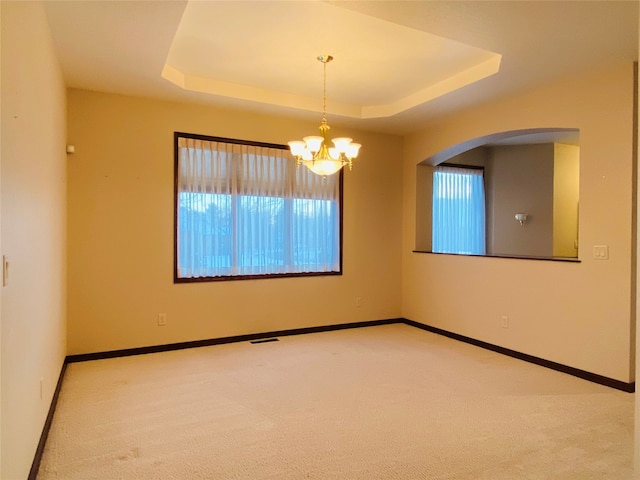 carpeted spare room with a tray ceiling and an inviting chandelier