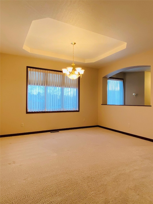 carpeted empty room featuring a notable chandelier and a tray ceiling