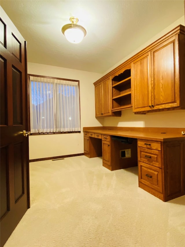 unfurnished office featuring built in desk and light colored carpet