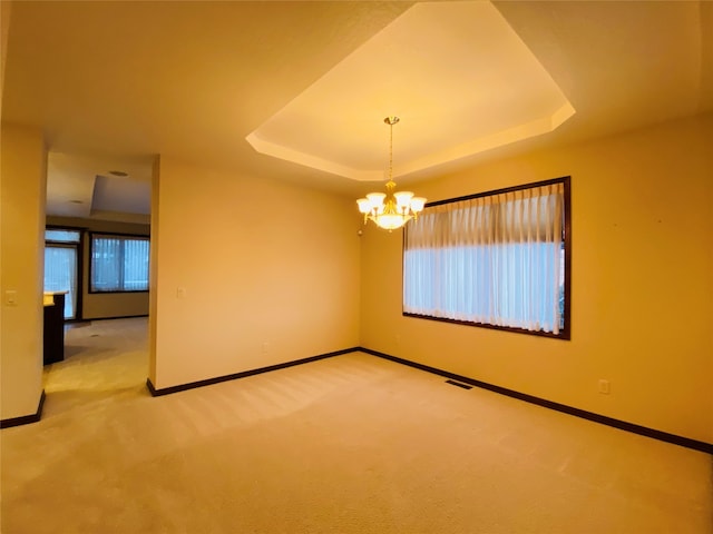 carpeted empty room with an inviting chandelier and a raised ceiling