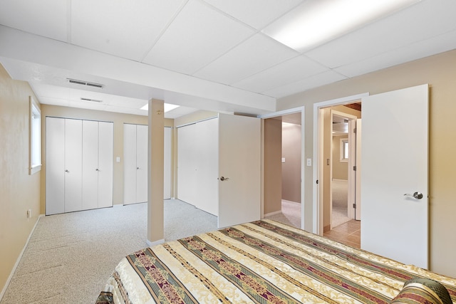 unfurnished bedroom featuring light carpet, a drop ceiling, and two closets