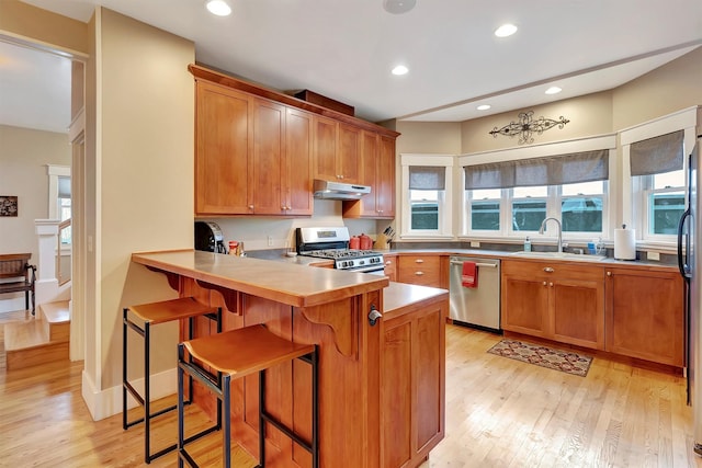 kitchen with a kitchen bar, stainless steel appliances, sink, kitchen peninsula, and light hardwood / wood-style flooring