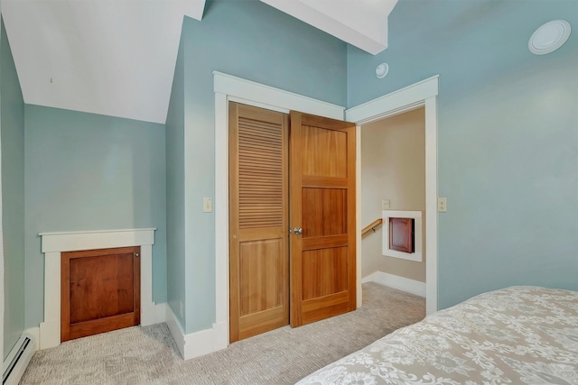 bedroom with a baseboard heating unit, a closet, light carpet, and vaulted ceiling