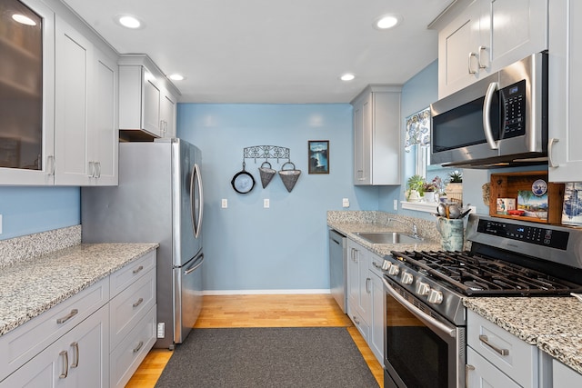 kitchen with sink, light stone countertops, light hardwood / wood-style flooring, and appliances with stainless steel finishes