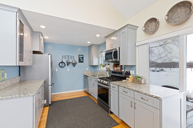 kitchen with light stone counters, light wood-type flooring, stainless steel appliances, and vaulted ceiling