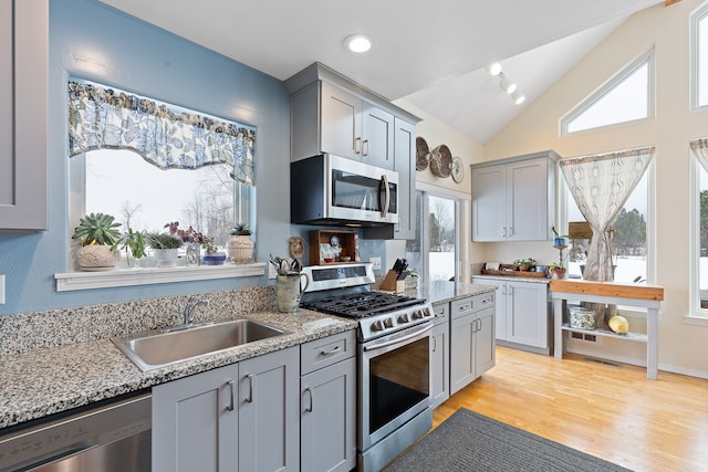 kitchen with light stone countertops, sink, stainless steel appliances, plenty of natural light, and lofted ceiling