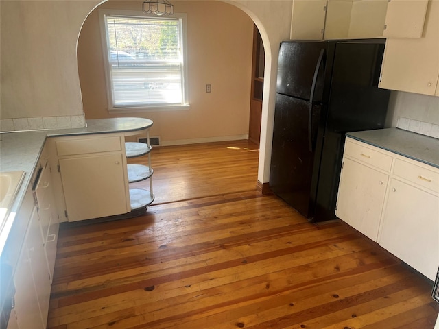 kitchen featuring arched walkways, light wood finished floors, freestanding refrigerator, and white cabinetry