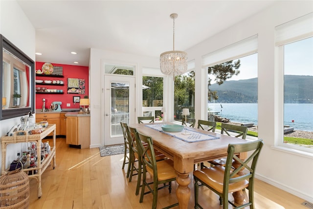 dining area featuring a water view, an inviting chandelier, and light hardwood / wood-style floors