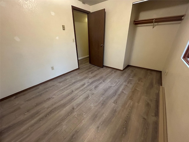 unfurnished bedroom featuring baseboard heating, a closet, and light wood-type flooring