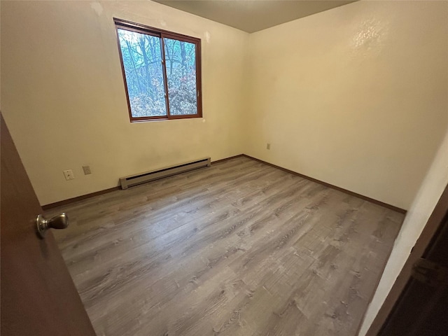 empty room featuring wood-type flooring and a baseboard heating unit